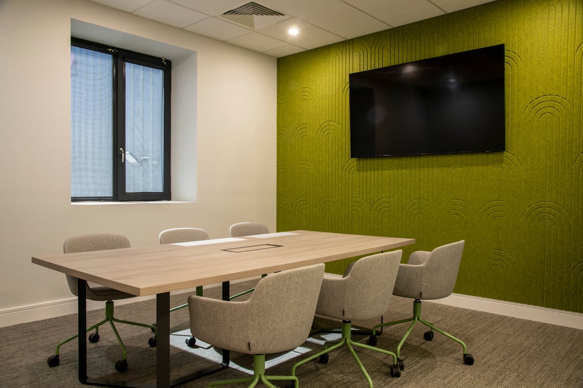 Modern office conference room with wooden table, beige chairs, green accent wall, wall-mounted TV, and window