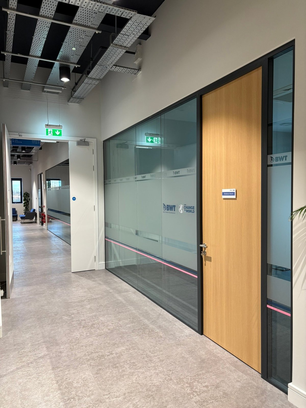 Modern office hallway with glass and wood partition walls, emergency exit sign, and minimalist interior design