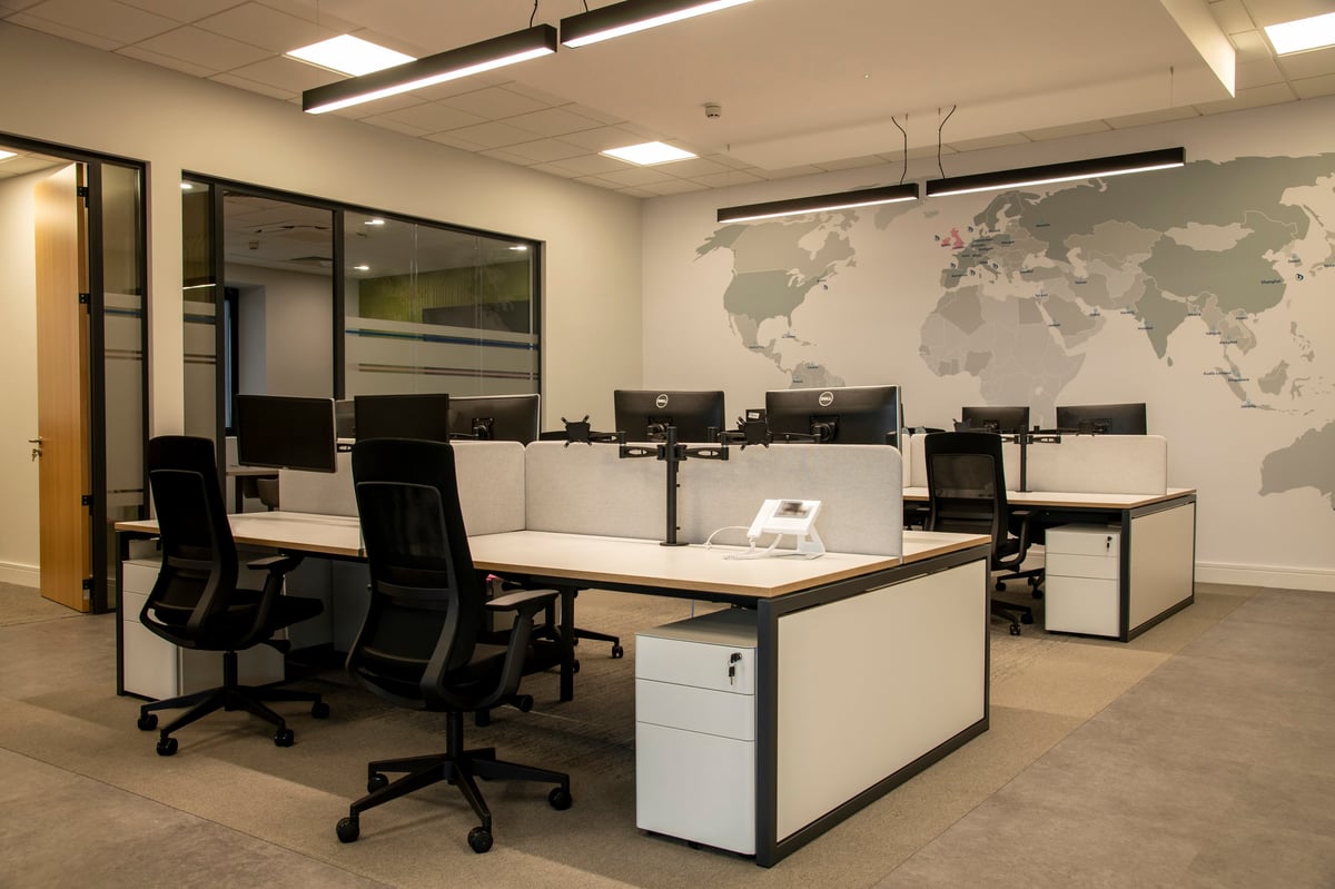 Modern office space with beige workstations, black office chairs, and world map decal on white wall